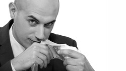 Businessman in suit holding and examining paper currency close to his face.