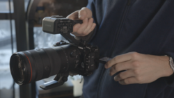 Videographer operating professional cinema camera with attached monitor and telephoto lens