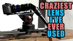 Robotic camera gimbal mounted on a wooden table with a DSLR and telephoto lens attached.