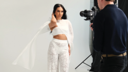 Model in white crop top and patterned pants poses during studio photoshoot with camera operator
