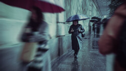 Person with umbrella walking through wet cobblestone alley with blurred figures and buildings