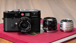 Leica M camera body with three interchangeable lenses displayed on a pink book.