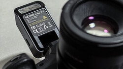 Compact camera flash unit with yellow label mounted on camera body next to telephoto lens.