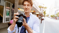 Photographer holding a DSLR camera on an urban street, demonstrating equipment handling.