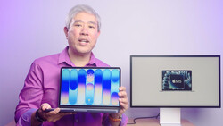 Man in magenta shirt displaying laptop with blue gradient wallpaper beside monitor showing M5 chip graphic.