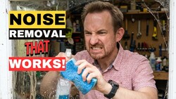 Man in pink shirt demonstrating noise removal technique with blue textured material in workshop setting.