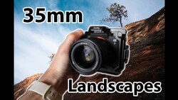 Hand holding a camera with a 35mm lens pointed at a rocky landscape with sparse vegetation.