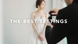 Bride in white strapless gown posing while photographer frames shot with camera.