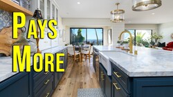 Modern kitchen with marble island countertop, dark blue cabinetry, and brass fixtures overlooking coastal views.