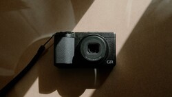 Ricoh GR compact digital camera viewed from above with natural window light casting shadows.