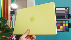 Yellow MacBook held open in a studio with color reference charts visible in the background.