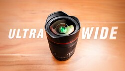 Ultra-wide camera lens with green lens element displayed against warm orange wooden background.