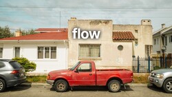 Red pickup truck parked between two cars on a residential street with aging buildings.