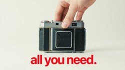 Hand holding a vintage folding camera with squared-off design against a neutral background.