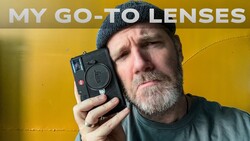 Photographer holding a compact rangefinder camera against a yellow background.