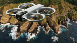 Quadcopter drone hovering above rocky coastal cliffs with crashing waves below.