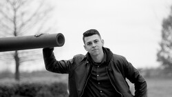 Man in black leather jacket holding metal pipe over shoulder in monochrome outdoor portrait