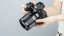 Hands holding a mirrorless camera with attached telephoto lens against gray background