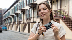 Woman holding a vintage film camera on a European street lined with classical architecture
