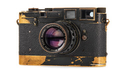 Weathered vintage rangefinder camera with worn brass trim and purple-tinted glass lens element.
