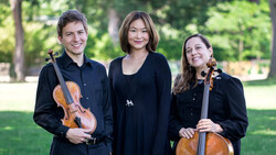 Three musicians in black clothing posing outdoors with violin and cello
