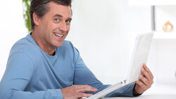 Man in blue long-sleeve shirt smiling while holding and looking at a tablet device.