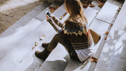 Child sitting on white papers outdoors, holding a striped object, viewed from above with natural shadows.