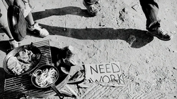 Overhead shot of person sitting on pavement with food and sign reading "NEED WORK"