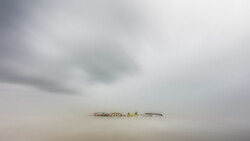 Minimalist landscape with industrial structure barely visible through dense fog and mist
