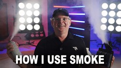 Man in glasses and black cap demonstrating lighting technique in front of professional LED panel array.