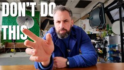 Videographer in blue jacket gesturing toward camera in studio setting with warning text overlay.