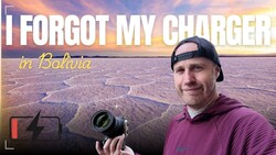 Photographer holding a camera with a depleted battery indicator, standing in front of a vast salt flat at sunset.