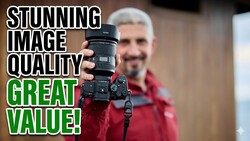 Photographer holding a mirrorless camera with attached telephoto lens toward the camera.