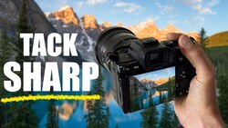 Hand holding a mirrorless camera displaying a sharp landscape photo of a mountain lake on its rear screen.