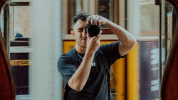 Male photographer looking through camera viewfinder in indoor space.