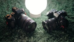 Two professional mirrorless cameras positioned on green textured fabric with a bright circular light source above.