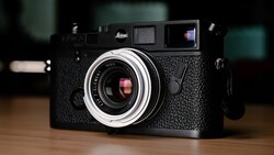 Black Leica rangefinder camera with chrome lens and textured body on wooden surface.