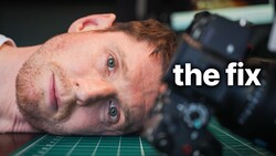 Man lying on desk with camera gear, looking at camera with tired expression labeled 'the fix.'