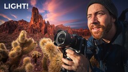 Photographer holding a cinema camera in a desert landscape with dramatic sunset sky and cacti.