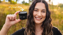 Photographer holding a compact camera lens outdoors with a blurred field background.