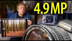 Photographer holding printed forest landscape photo next to Olympus lens and camera equipment on desk.