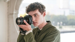 Young photographer holding DSLR camera with telephoto lens to eye while looking toward camera
