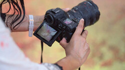 Photographer holding a DSLR camera with a telephoto lens in muddy conditions outdoors