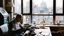 Man working at typewriter at desk overlooking urban skyline through large windows