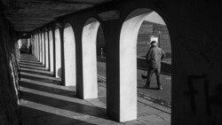 Worker walking through brutalist concrete underpass with strong leading lines and geometric shadows