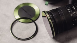 Camera lens with green-tinted filter and protective ring laid out on gray surface