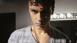Portrait of young man with curly dark hair wearing gray shirt and chain necklace