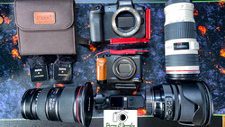 Overhead flat lay of camera gear including mirrorless camera body, lenses, speedlight flash, batteries, and accessories on patterned fabric