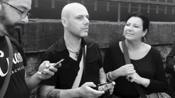 Three people sitting on concrete steps in black and white, engaged in conversation while holding mobile devices