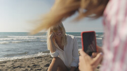 Woman posing for a smartphone photo on a beach at golden hour